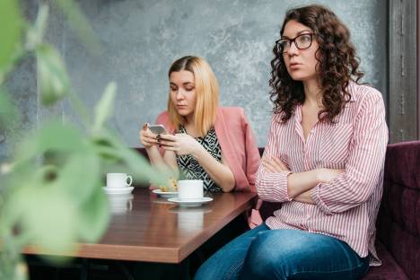 Zwei junge Frauen treffen sich, aber die eine schaut nur auf ihr Smartphone