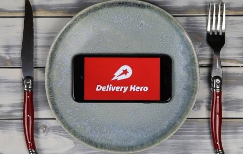 Delivery Hero App aus Smartphone, im Hintergrund Teller und Besteck