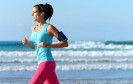 Frau joggt am Meer mit Smartphone